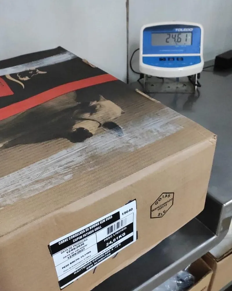 Caixa de 24,61 kg na balança, com a etiqueta marcando o mesmo peso líquido